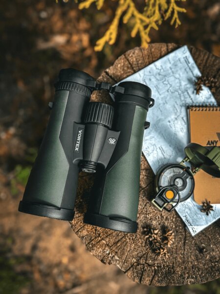 Outdoor binoculars placed on a tree stump with a map and hiking gear. Photo: Rigad