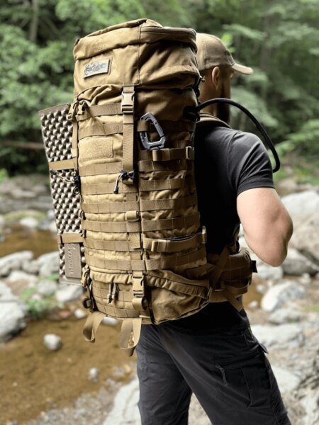 Hiker with a large expedition backpack by a mountain stream in the forest. Photo: Rigad.