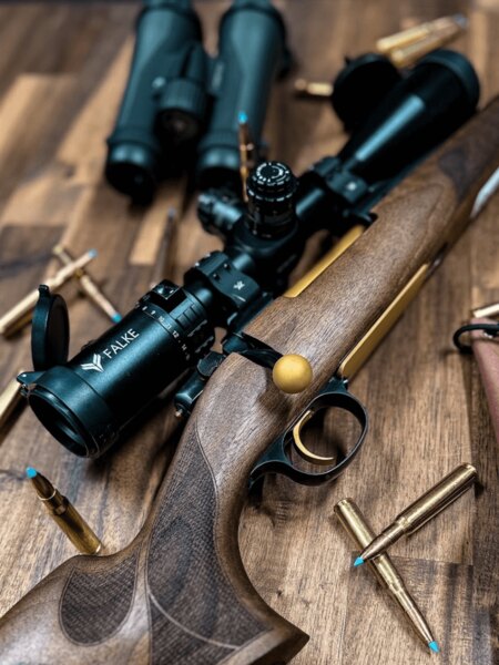Falke riflescope mounted on a hunting rifle with a wooden stock, cartridges placed on the table. Photo: Rigad