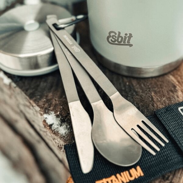 Esbit titanium cutlery set (spoon, knife, and fork) placed beside an outdoor thermos on a wooden surface. Photo by Rigad.