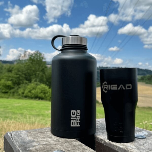 Black thermos bottle Big Frig and Rigad mug on a table in a natural setting with a view of the landscape. Photo: Rigad