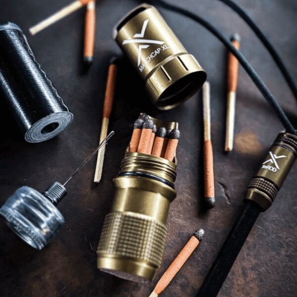 Golden capsule Exotac Matchcap XL open with stored matches and accessories on a dark background. Photo: Rigad