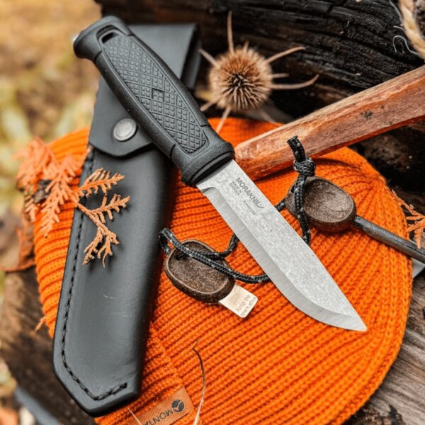 Outdoor knife Morakniv with a black sheath and fire starter on an orange mat in nature. Photo: Rigad