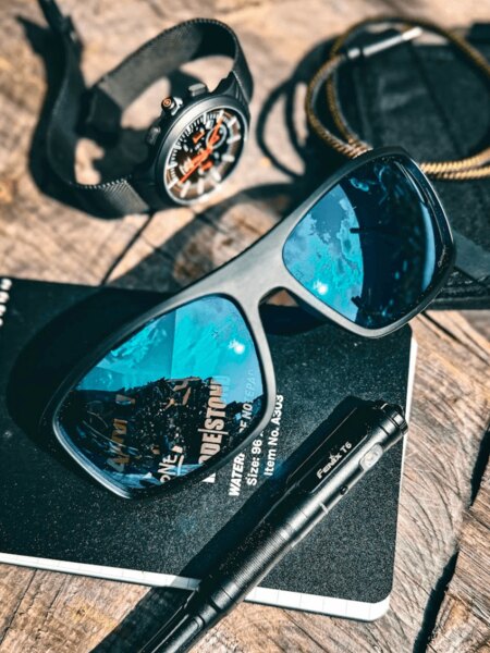 Sunglasses with polarized lenses Wiley X on the table with a watch, tactical notebook, and flashlight
