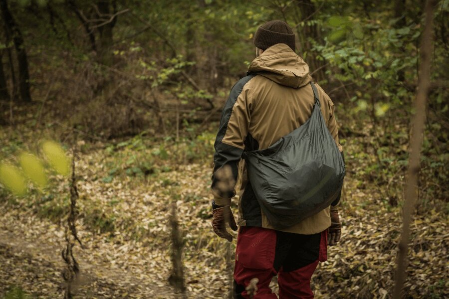 Moving through forest terrain in the rain while protecting equipment with a waterproof dry bag, illustrating preventive gear protection in wet field conditions. Photo: Helikon-Tex, Rigad