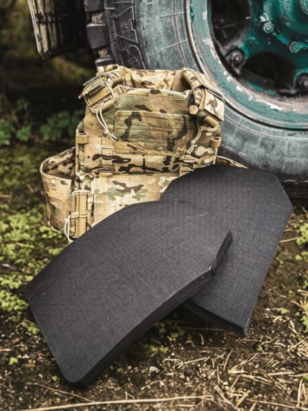 Pair of curved ballistic plates (multi-curve) on a carrier in multicam pattern; outdoor environment by the vehicle wheel.