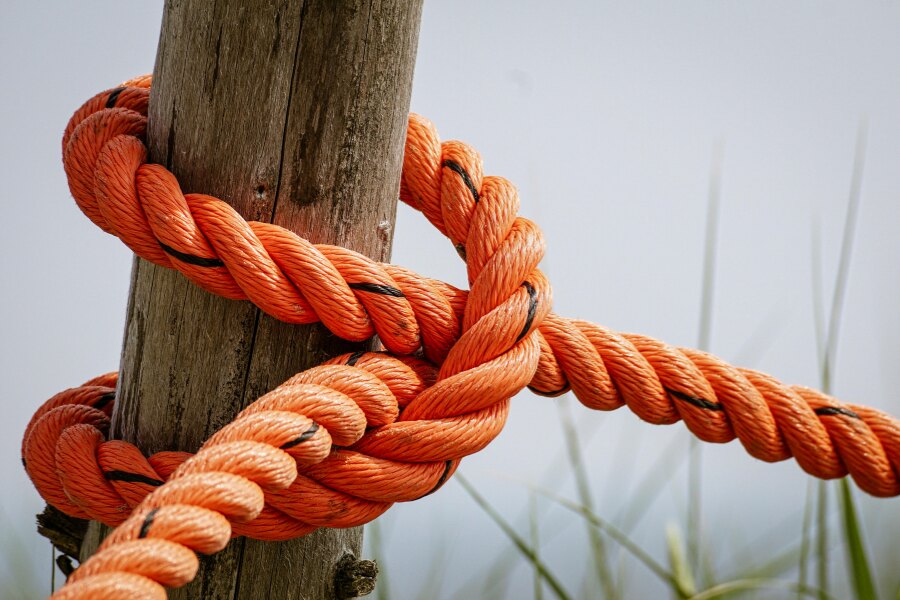 Strong orange rope tied to a wooden post in a simple knot.