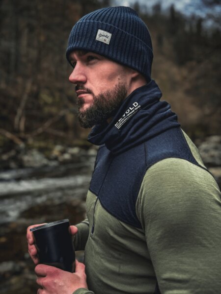 Man in winter nature dressed in Devold merino thermal wear, with a scarf and hat, holding a thermal mug. Photo: Rigad