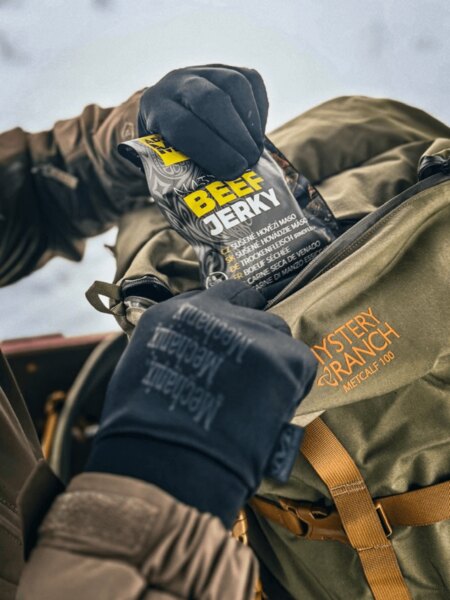 Hand in Mechanix winter gloves takes out a pack of beef jerky from the pocket of a Mystery Ranch backpack during a break on a winter hike. Photo: Rigad