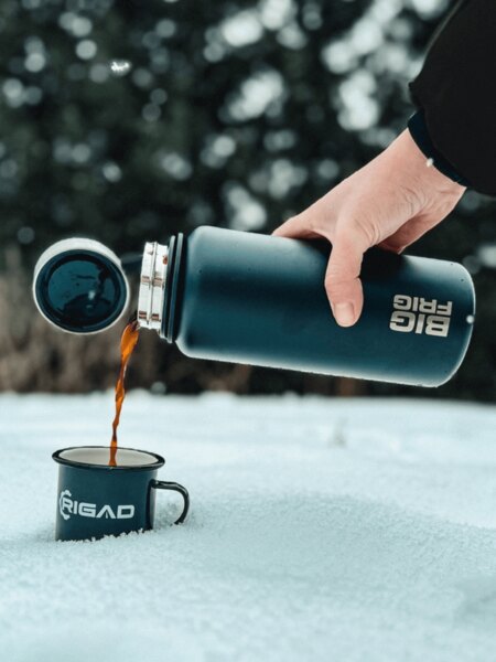 Tourist pours a warm drink from a thermos into a mug in the snow. Photo: Rigad