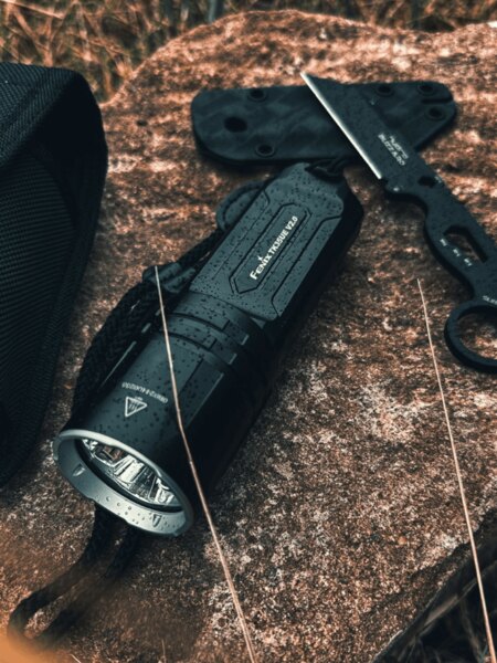 Fenix® TK35 Ultimate Edition tactical flashlight on a wet rock in an outdoor environment. Photo: Rigad