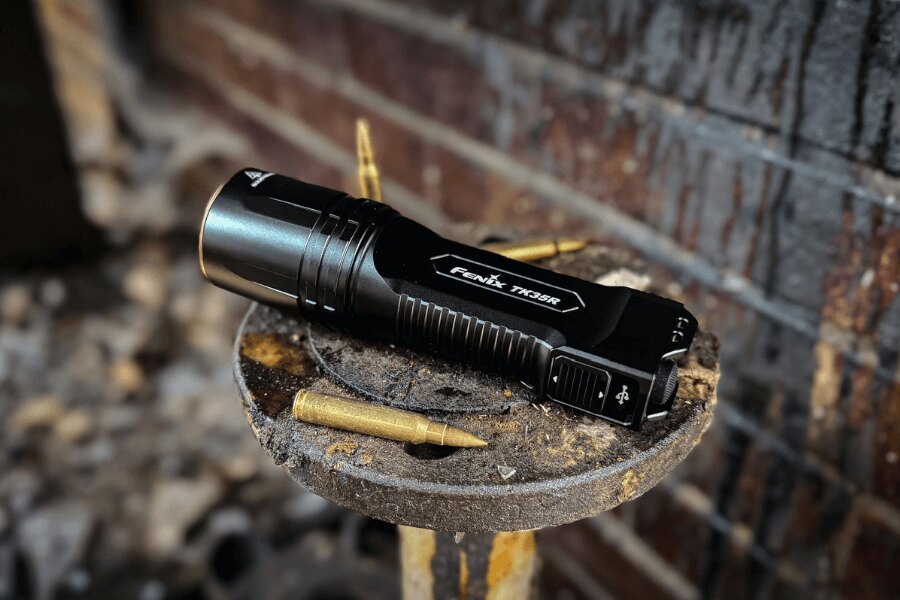 Fenix® TK35R high-performance tactical flashlight placed on a metal surface with ammunition. Photo: Rigad