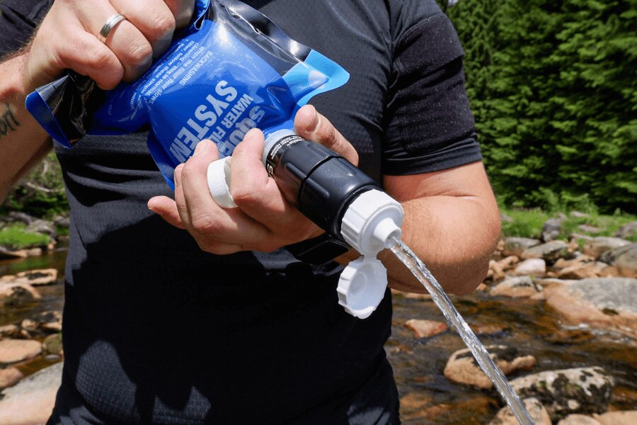 A person using a Sawyer squeeze filter to press water from a reservoir in the outdoors. Photo: Rigad