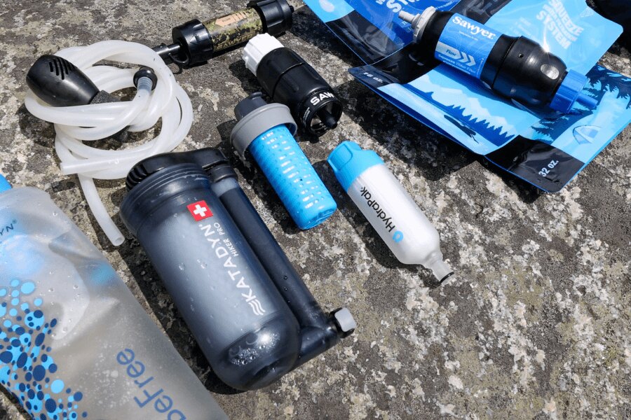 A selection of portable water filters from Sawyer, HydraPak, and Katadyn displayed on a stone surface. Photo: Rigad