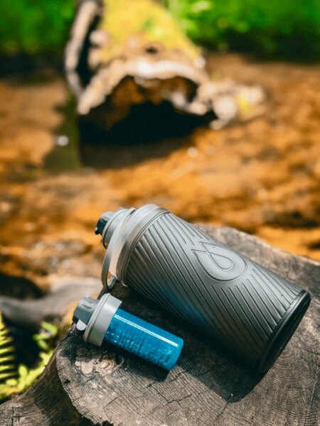 Flux HydraPak bottle with Cap filter resting on a tree stump in nature, ideal for travel and outdoor use. Photo: Rigad.