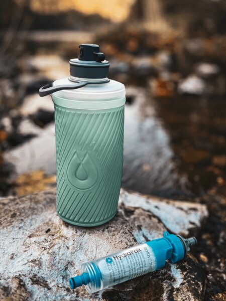 Collapsible Flux™ HydraPak<sup>&reg;</sup> bottle with attached HydraPak<sup>&reg;</sup> Water Filter (28 mm), placed on a rock by a stream. Photo: Rigad.