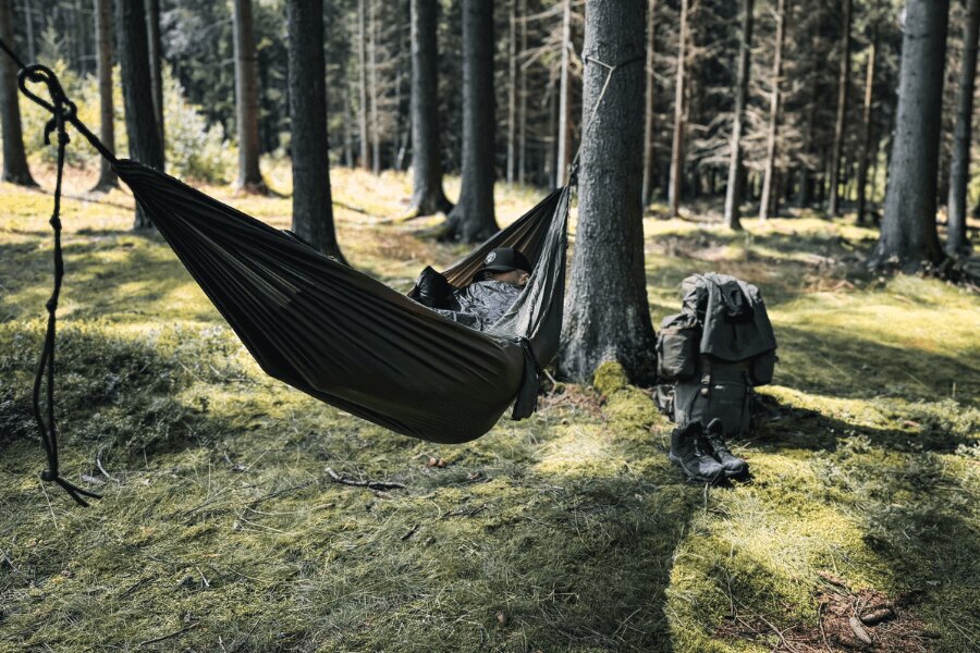 Hammock used as a sleeping system in the forest, outdoor gear and a backpack ready next to the hammock. Photo: Rigad