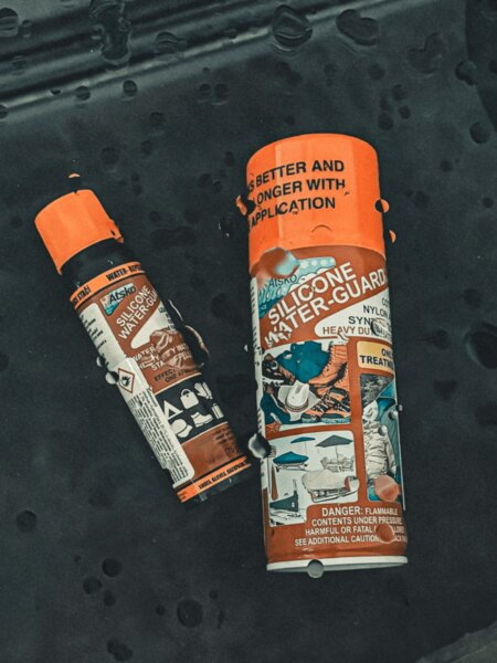 Atsko Silicone Water-Guard waterproofing sprays on dark fabric covered with water droplets.