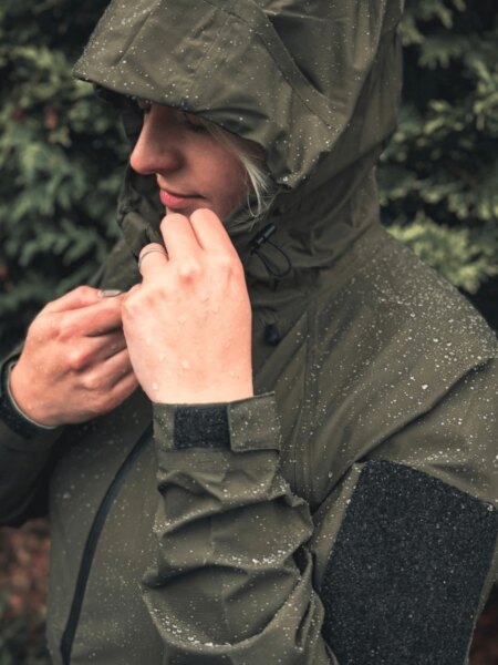 Woman wearing a Helikon-Tex Squall waterproof jacket, with water droplets on the hood and sleeves.