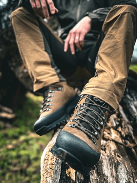 Brown Hanwag leather hiking boots resting on a tree trunk in a forest.