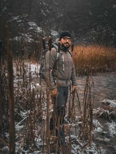 Man wearing winter outdoor clothing and carrying a backpack in a snow-covered wetland.
