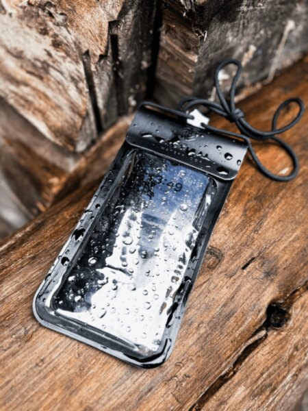 Mobile phone inside a Tactical waterproof pouch covered with water droplets on wet wood.