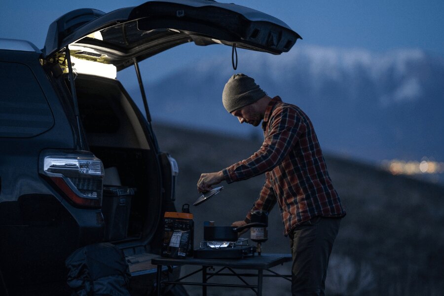 Man cooking next to an SUV during a mountain getaway, symbolizing remote-controlled smart home security. Photo: Rigad