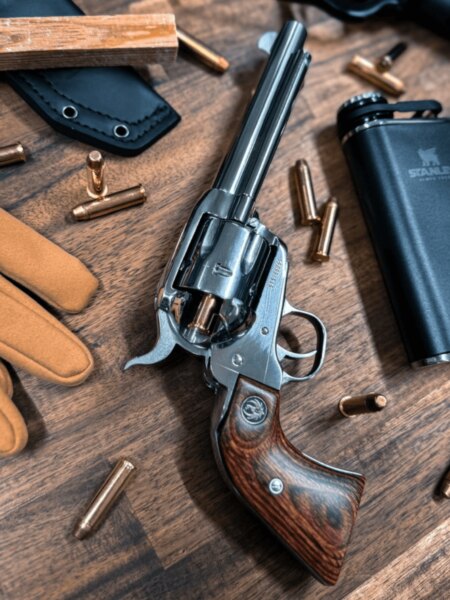 Long-barreled Ruger single-action revolver with wooden grips placed among cartridges and outdoor gear.