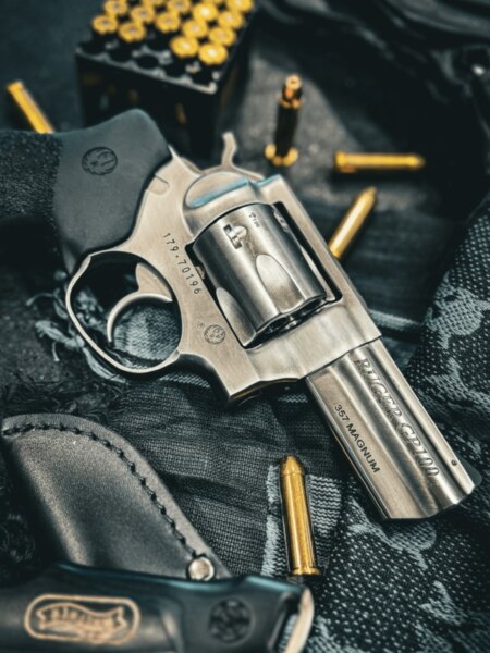 Ruger GP100 revolver in .357 Magnum placed beside cartridges and a shooting holster.