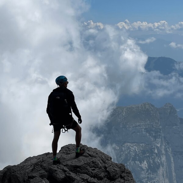 Tourist above the clouds during a high-altitude hike, standing at the summit overlooking the alpine landscape. Source: Rigad
