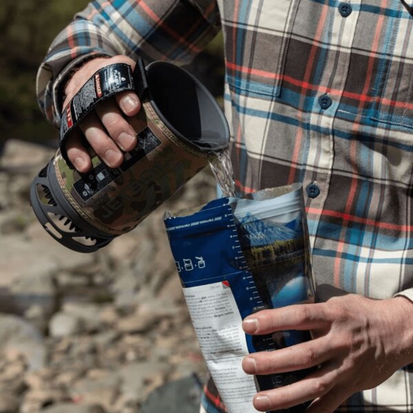 A man pours hot water from a Jetboil stove into an MRE emergency meal outdoors. Photo: Rigad