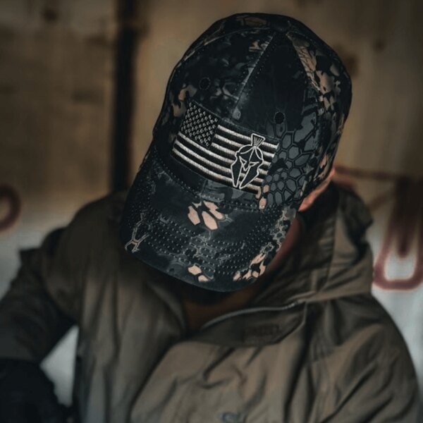 Close-up of a Kryptek cap featuring an American flag and Spartan emblem, worn indoors. Photo by Rigad.