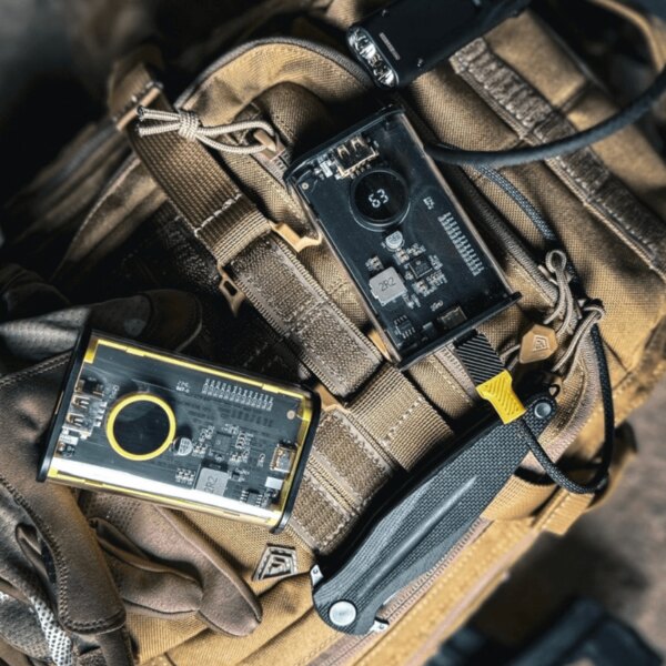 Tactical<sup>&reg;</sup> C4 Explosive Power Bank, 9600 mAh placed on tactical gear; transparent body with display, fast charging, and rugged field-ready design. Photo: Rigad.