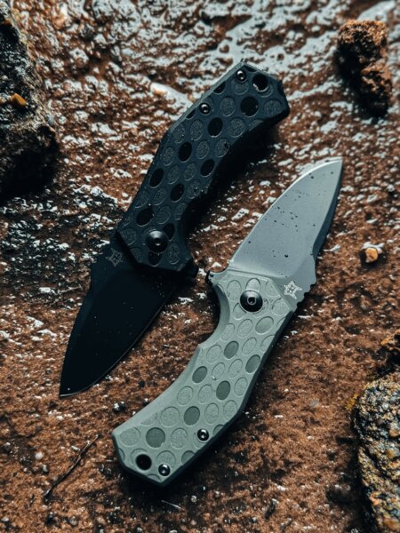 Pair of Fox Knives® folding knives with black and green handles in an outdoor setting. Photo: Rigad