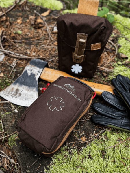 Helikon-Tex Bushcraft Medical Kit in a brown case, placed in the forest by an axe and gloves – first aid kit for bushcraft and outdoor. Photo: Rigad.