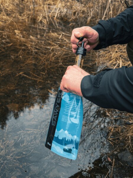 Water filtration using a portable Sawyer filter in nature – water treatment for safe drinking during bushcraft activities. Photo: Rigad