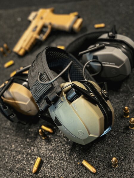 Active shooting earmuffs with low-profile ear cups placed on the shooting range next to the ammunition and pistol. Photo: Rigad