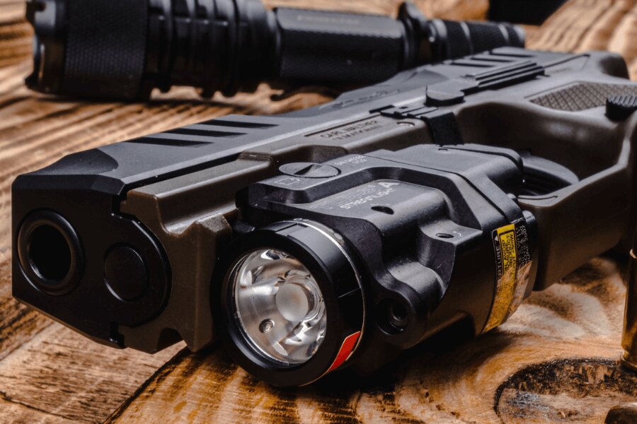 Detail of a black pistol with an under-barrel LED flashlight and Picatinny rail mount – Photo: Rigad