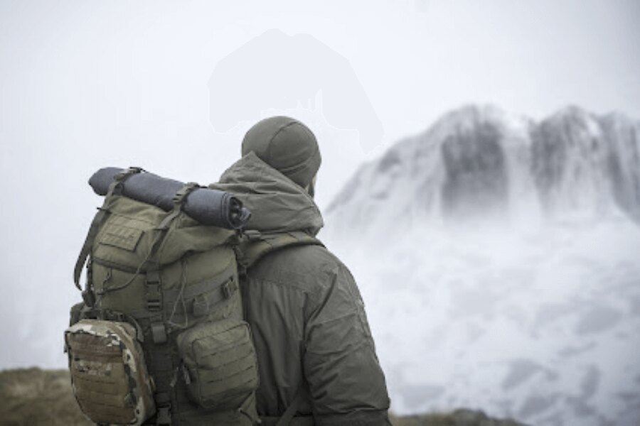 Man with a backpack standing in foggy mountain terrain, remote environment with no visible signs of civilization.