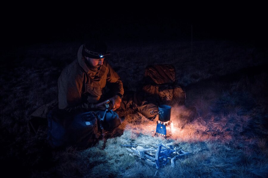 Man wearing a headlamp preparing equipment at night in mountainous terrain.