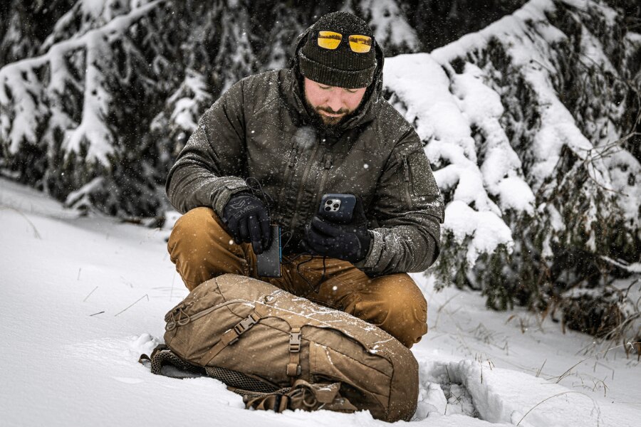 A man using a mobile phone connected to a power bank in snowy winter conditions. Photo: Rigad