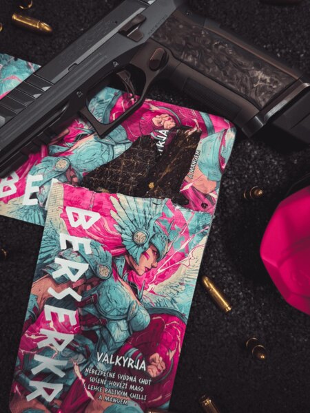 Berserkr VALKYRJA Mango &amp; Chilli beef jerky packaging with a visible slice of jerky, photographed alongside a firearm and ammunition.
