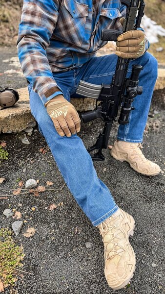 Man seated with a rifle wearing Treadstone Jeans<sup>&reg;</sup> Helikon-Tex<sup>&reg;</sup> during outdoor use. Photo: Rigad