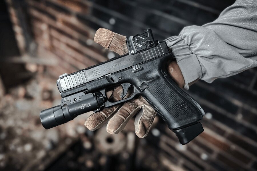 Glock 45 pistol with an Aimpoint COA red dot sight and a weapon-mounted light in the shooter’s hand. Photo: Rigad
