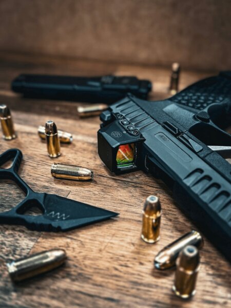 SIG Sauer pistol with a slide-mounted red dot sight resting on a wooden table among 9 mm cartridges. Photo: Rigad
