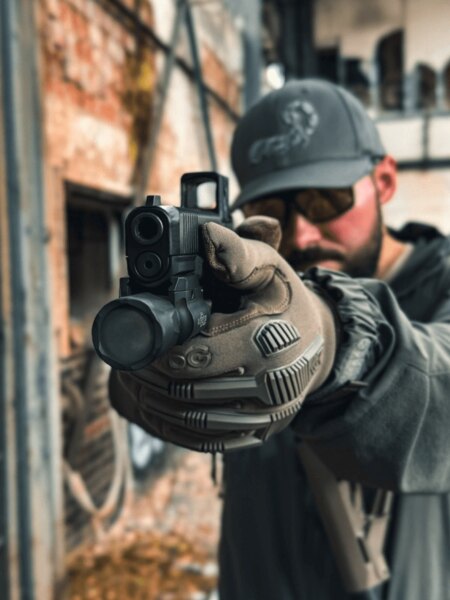 Shooter aiming with a Glock pistol equipped with an Aimpoint COA red dot, real-world shooting perspective. Photo: Rigad