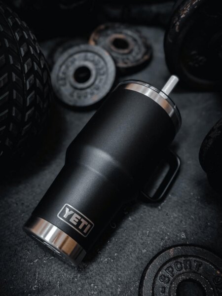Black YETI Rambler tumbler placed among weight plates in a gym