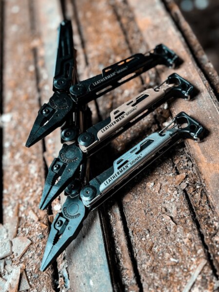 Three Leatherman Signal multitools in different colour options displayed on a wooden surface.