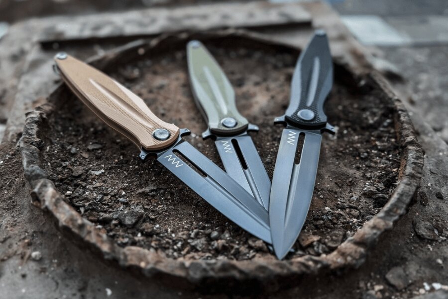 Three ANV folding knives in different color variants placed on a metal surface.