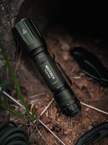 Nextorch TA30C MAX compact flashlight placed on the ground in an outdoor environment.
